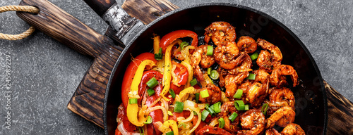 shrimp fajitas with bell pepper and onion cooked in a frying pan, top view, banner