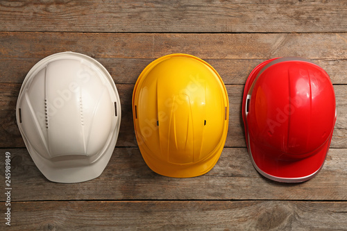 Different hard hats on wooden background, top view. Safety equipment