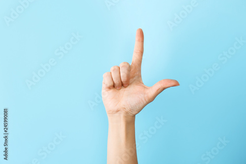 Woman showing L letter on color background, closeup. Sign language