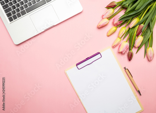 Pink tulips bouquet, blank notepad and computer laptop on pink pastel background, top view