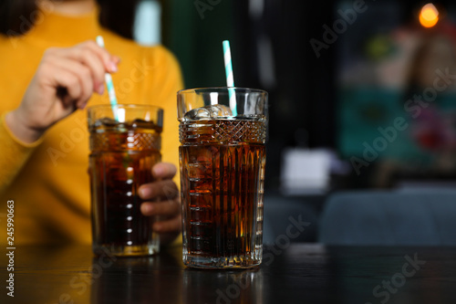 Glass of refreshing cola and blurred woman on background. Space for text