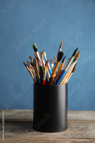 Holder with paint brushes on table against color background