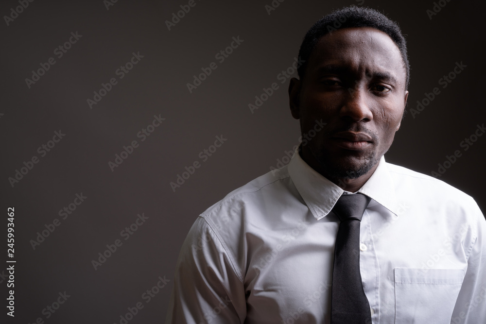 Fototapeta premium Young handsome African businessman against gray background