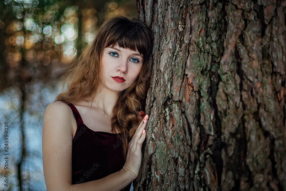 Portrait of a beautiful girl in a dark long dress who stands alone among the trees in the winter forest Portrait of a beautiful girl in a dark long dress who stands alone among the trees in the winter forest