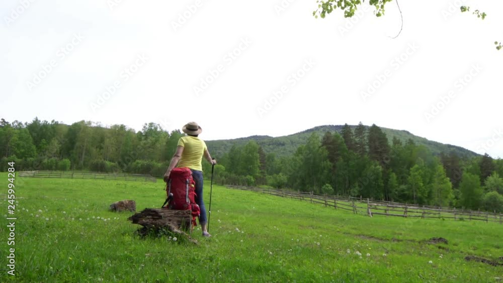 The woman the traveler with a red backpack and tourist sticks goes on the mountain area. The woman the traveler with a red backpack and tourist sticks goes on the mountain area.
