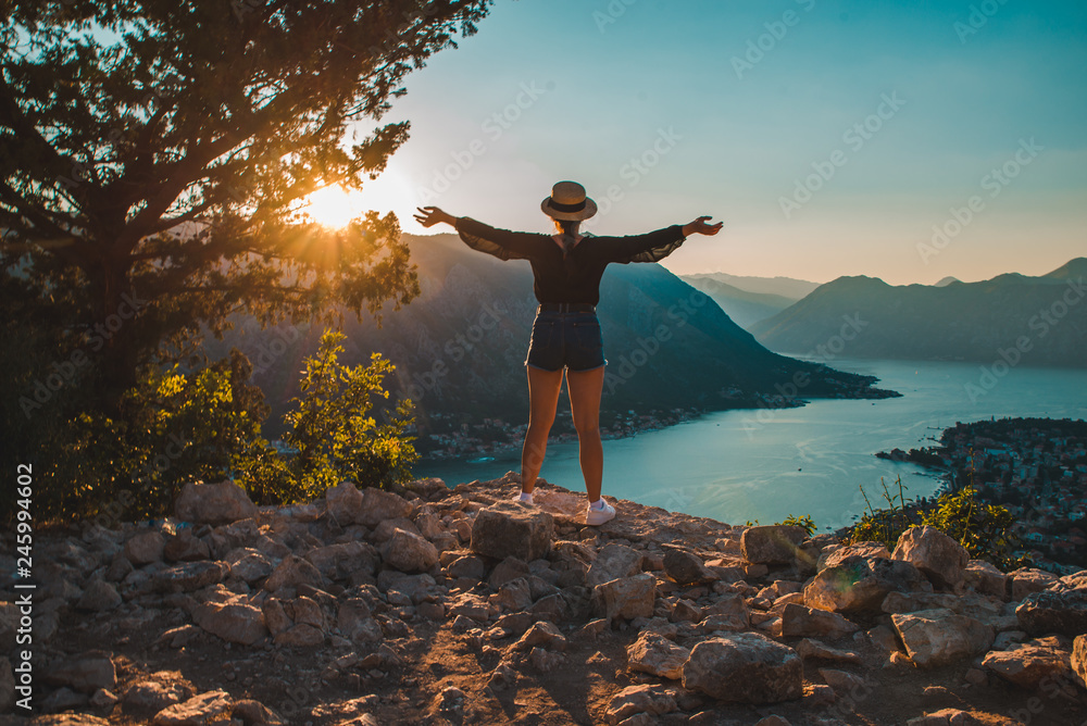 woman standing on the top of hill. kotor with sunset on background - obrazy, fototapety, plakaty 