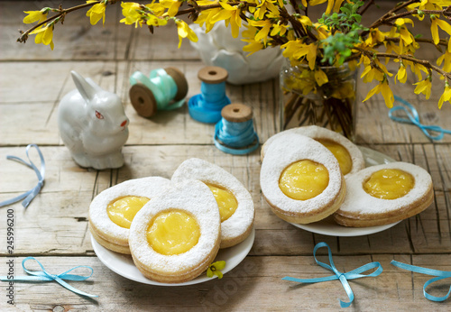 Easter composition with egg-shaped cookies filled with lemon curd, rabbit, bouquet of forsythia and bows. photo