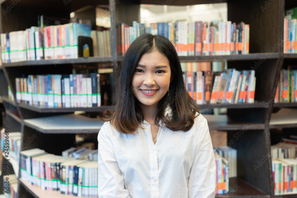 Happy young woman in the library with books to search information. Happy young woman in the library with books to search information.
