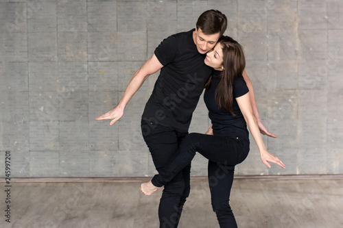 Modern style couple of dancers. Young man and woman in black suits practicing modern dance on studio background.