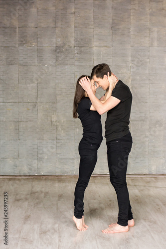 Couple of dancers in romantic position. Full length portrait of beautiful dancers wearing black suits hugging each other on grey background. Loving couple is dancing.