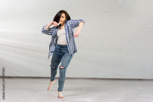 Young pretty dancer in dynamic pose. Beautiful energetic modrrn style girl dancing break dance on grey studio background. Young dancer in movement.
