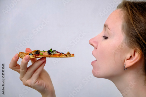 Happy young woman eating a piece of hot pizza on white background