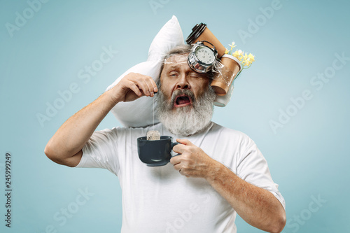 Surprised senior man drinking tea after sleeping at home or office having too much work. Bored businessman with pillow and hourglass. The busy, boring, worried, be late, concerned, sleep day photo