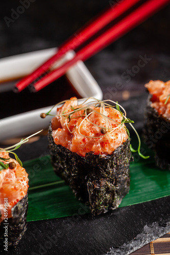 Gunkan Maki Sushi with with salmon on a bamboo leaf and on a black stone slate. Bamboo mat. red chinese sticks. Sushi menu. Japanese food. trend color 2019 coral. background image