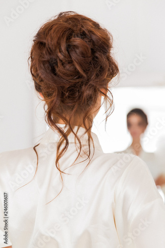 Back view of the happy bride who is looking at the mirror indoor