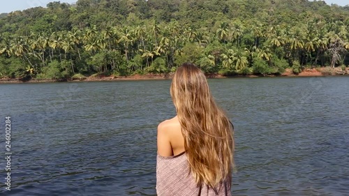 a woman stands with her back to the camera and looks across the river at the palm trees. Sunny pleasant day to relax.