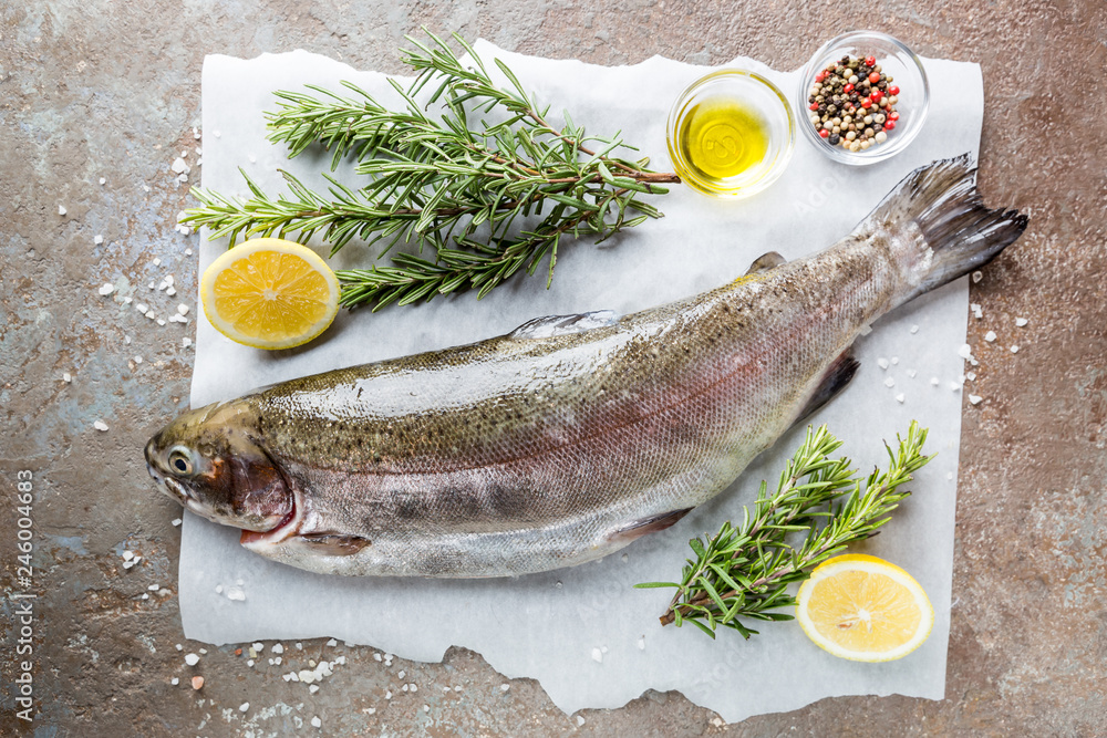 Raw trout fish on paper with rosemary and lemon on a stone table, top view Raw trout fish on paper with rosemary and lemon on a stone table, top view
