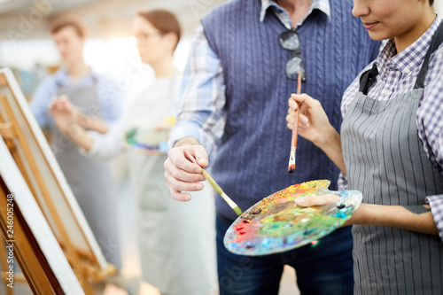 Mid section portrait of two unrecognizable artists holding palette mixing oil colors while painting picture on easel in art studio, copy space