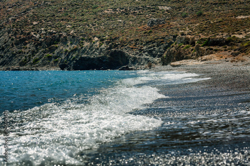 Seashore with foamy waves against the backdrop of the mountains, bright sunny day