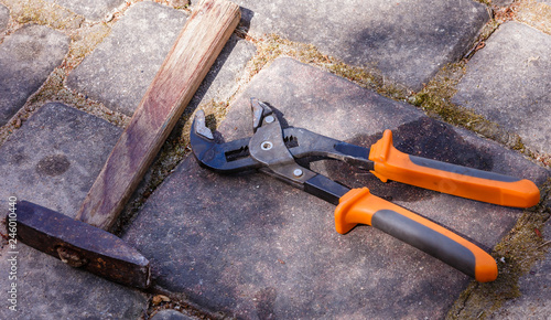 old tools on the pavement; iron hammer with wooden handle and plumber key with orange handles