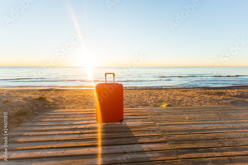 Luggage, holidays, travel concept - a red suitcase standing near the sea in sunlight