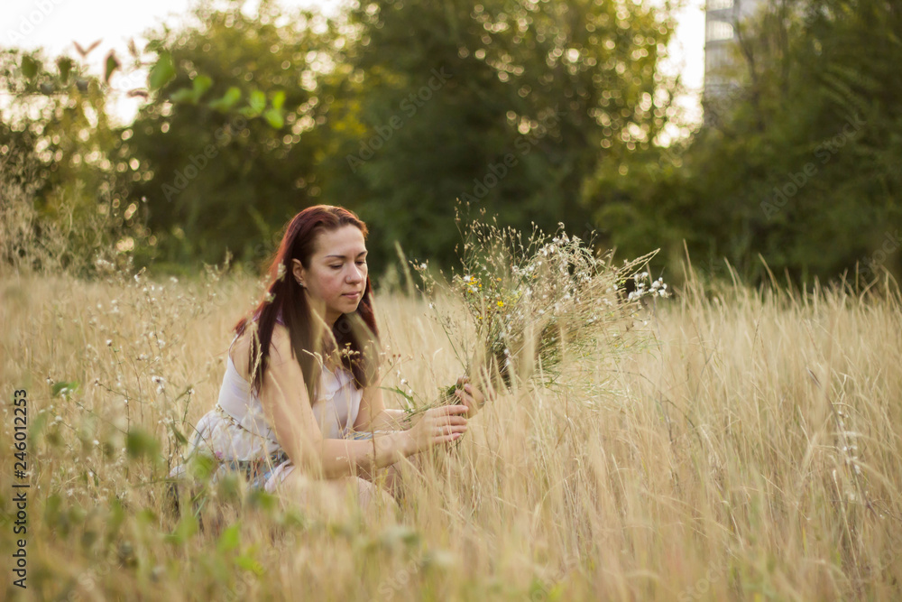 Pretty girl in a long light dress collects wild flowers Pretty girl in a long light dress collects wild flowers
