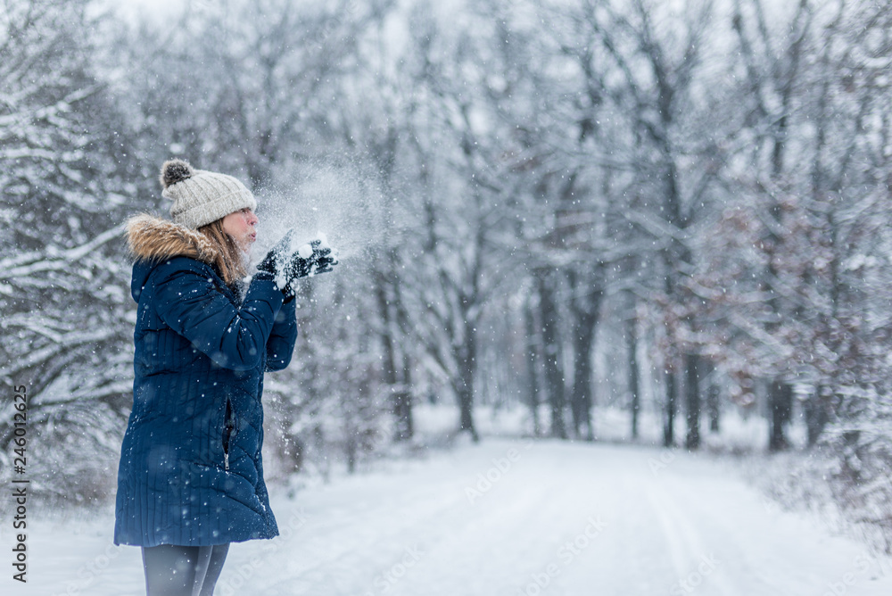 woman blowing handful of snow into the air in winter wonderland woman blowing handful of snow into the air in winter wonderland