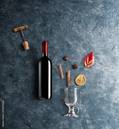 Mulled wine recipe ingredients and kitchen accessories, bottle of red wine, cinnamon, anise stars, orange, brown sugarand spice on blue stone background.