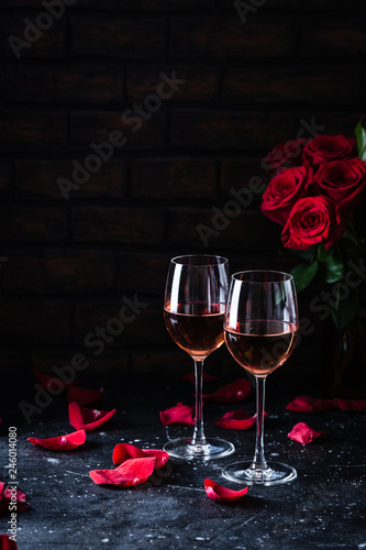 Obraz na plátně Two wine glasses of rose wine on brick background, bouquet of red roses for roma