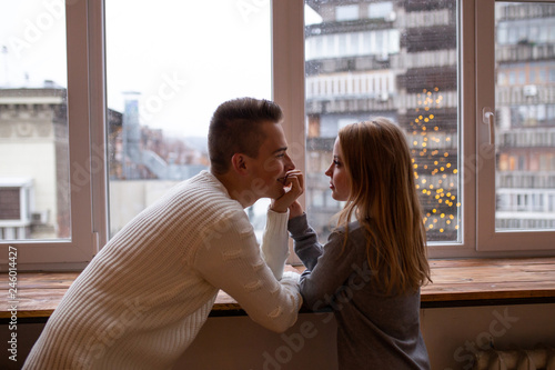 Beautiful young couple is talking and smiling at home near window