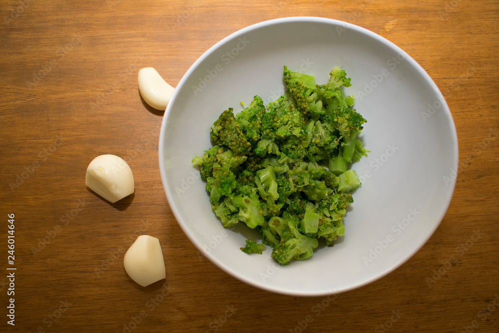 Bowl with chopped broccoli and garlic cloves. Bowl with chopped broccoli and garlic cloves.
