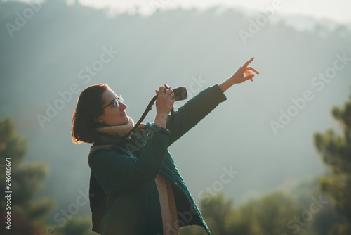 Happy photographer hiking taking picture of the nature and showing with a finger on a bird flying, hipster traveller doing phoography in a forest with green trees and beautiful view on the background photo
