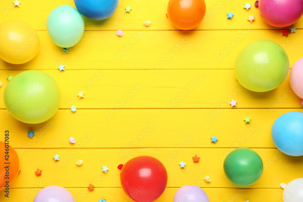 Colorful balloons with paper stars on yellow wooden table