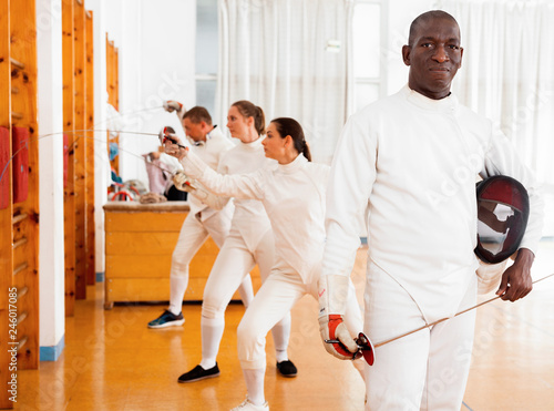 Active african american male fencer in uniform standing with mask and foil at fencing room