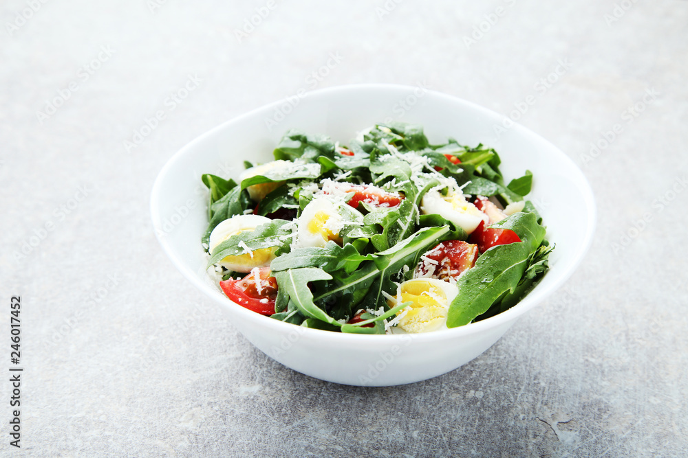 Salad with arugula leafs, tomatoes and eggs on grey wooden table