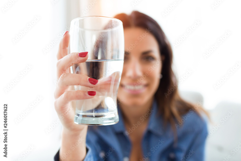 Pretty young woman smiling while looking at the camera through the glass of water at home. Pretty young woman smiling while looking at the camera through the glass of water at home.