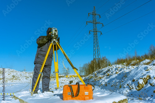 Surveyor in winter in overalls conducts a topographical survey for the cadastre