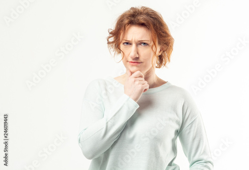 Beautiful red haired adult woman in casual looking into the camera with pensive expression, thinking or doubting about something on white background
