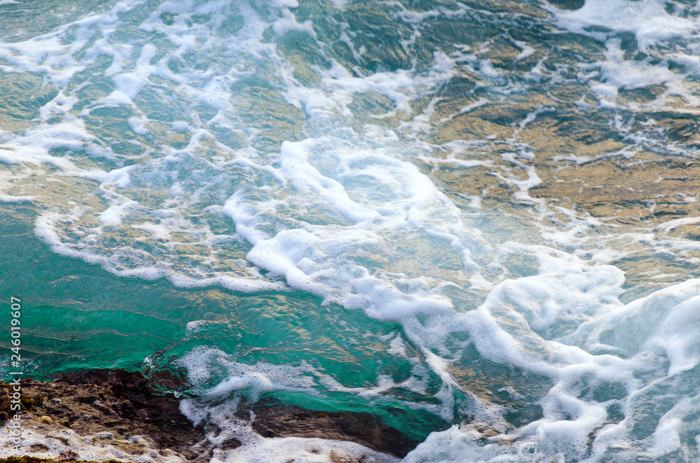 Turquoise sea water hits stony shore. Natural background. Photo with motion blur.