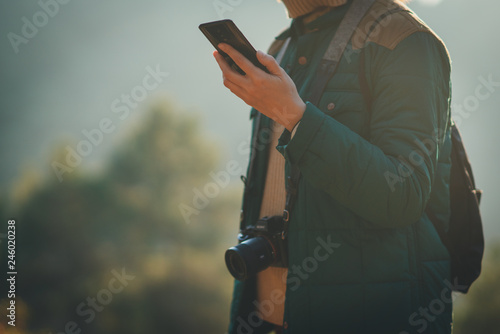 Crop picture of traveller girl with a photo camera holding cell telephone and checking the road in online map, copy space for your text and logo, blurred nature, trees and forest in the background