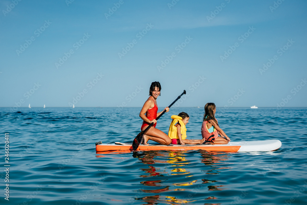 Φωτογραφία Mother with two daughters stand up on a paddle board