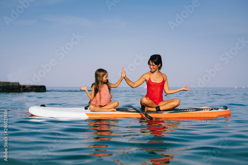 Mom and little daughter doing yoga on the paddle board © teksomolika