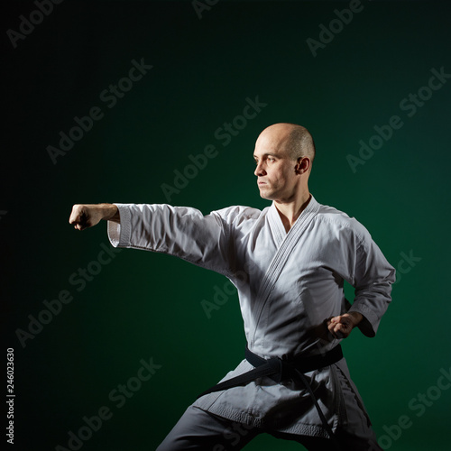 Against dark green background the athlete trains formal karate exercises