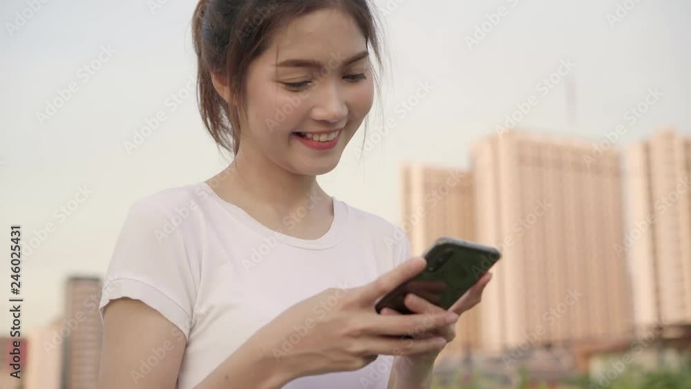 Cheerful Asian tourist blogger woman using touchscreen technology at smartphone while walking on the street at downtown city in the evening. Lifestyle backpack tourist travel holiday concept. Cheerful Asian tourist blogger woman using touchscreen technology at smartphone while walking on the street at downtown city in the evening. Lifestyle backpack tourist travel holiday concept.
