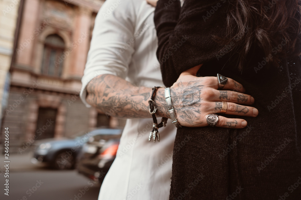 Φωτογραφία The man's hand in tattoos and jewelry embraces a girl's waist.