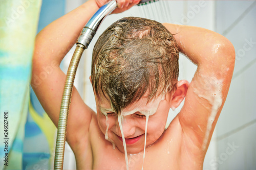 Fotografie The boy washes away the soapy hair in the shower with water.