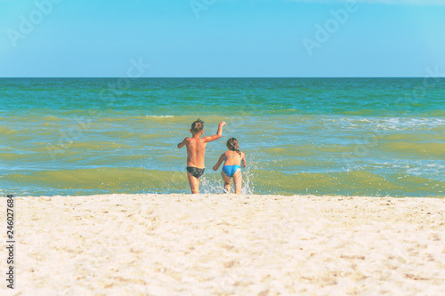 A boy and a girl are running along the beach, a brother and sister are running into the sea.