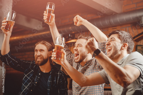Cheerful friends men fans watch sports match on TV and drink draft beer in bar pub photo