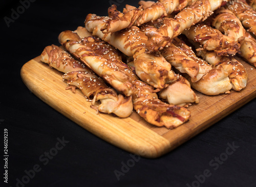 twisted cheese bread sticks with ham and sesame seeds on a wooden board on a black background