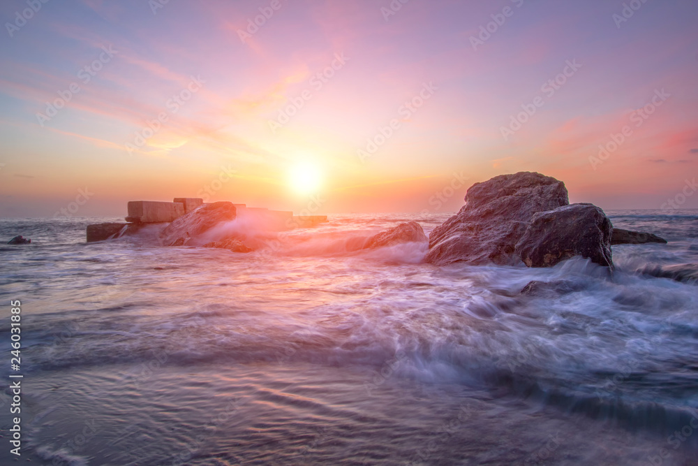 Naklejka premium Bright colorful sunrise on the beach. Sea waves in the bright rays of the sun